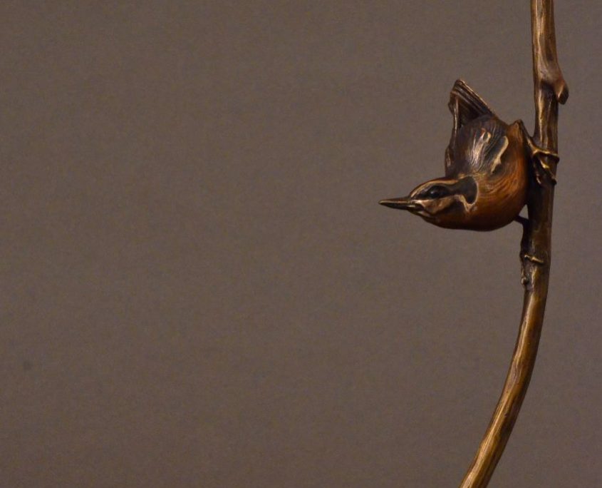 This is a bronze sculpture by Jim Green of a Red-breasted Nuthatch perched on a branch