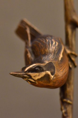 A bronze sculpture by Jim Green of a Red Breasted Nuthatch perched on a branch