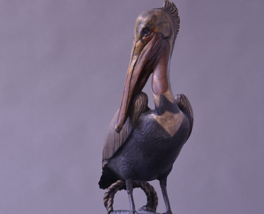 A bronze sculpture of a brown Pelican standing on a pier piling by Jim Green