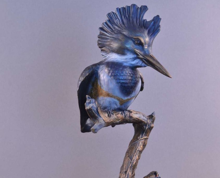 A bronze sculpture by Jim Green of a female King Fisher perched on a branch.