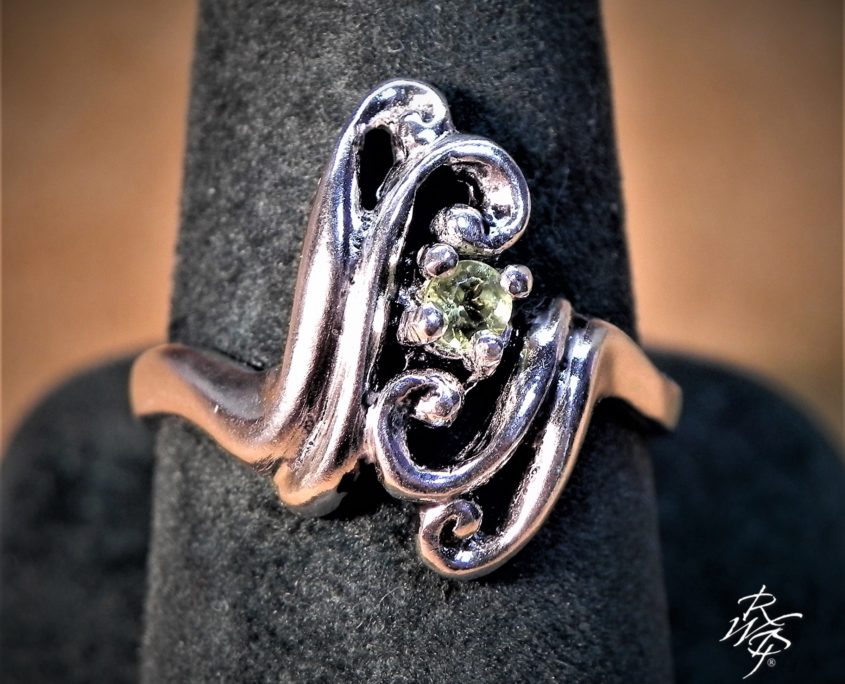 3 mm Peridot set in sterling silver prong setting in a scroll design. Western art inspired design.